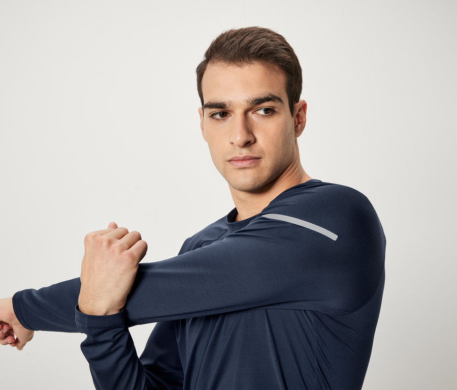 Férfi nyújtja a karját sötétkék hosszú ujjú sportfelsőben.