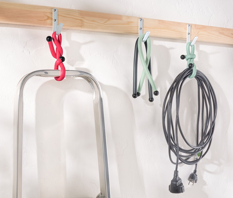 Egy létra áll egy fa léc alatt, melyen horgok vannak, melyekről piros, zöld és fekete Power Kabelbinder lóg.