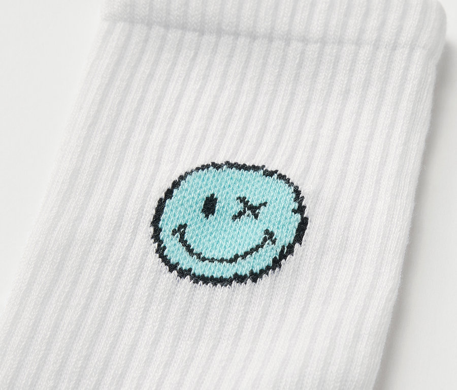 Egy fehér SMILEYWORLD® gyerek tenisz zokni részlete kék mosolygós mintával.