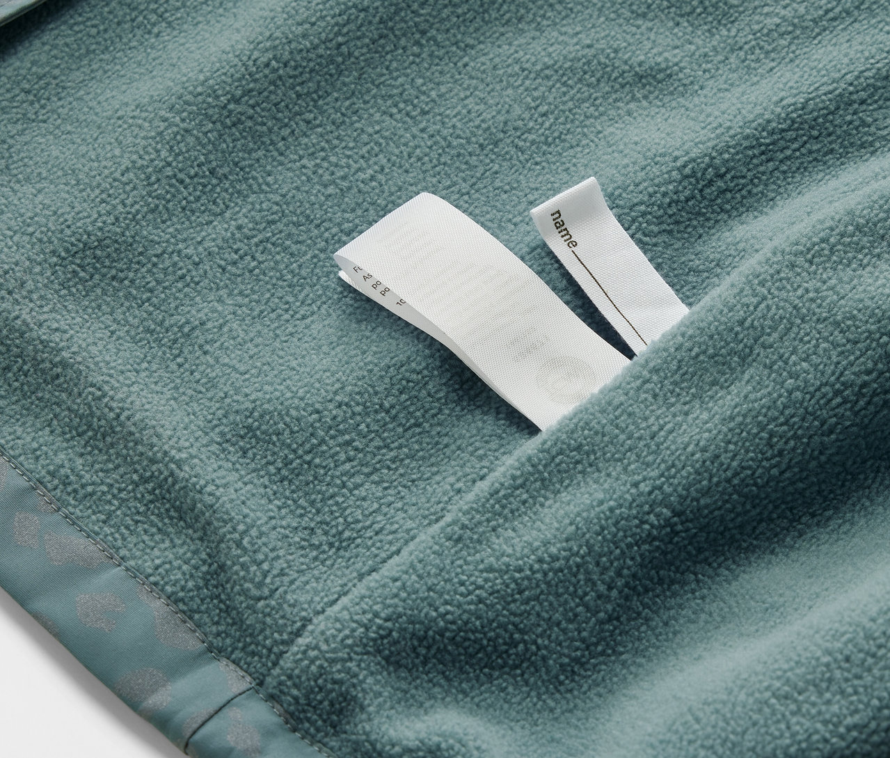 Egy gyerek termo esőkabát részlete fényvisszaverő elemekkel és névcímkével.