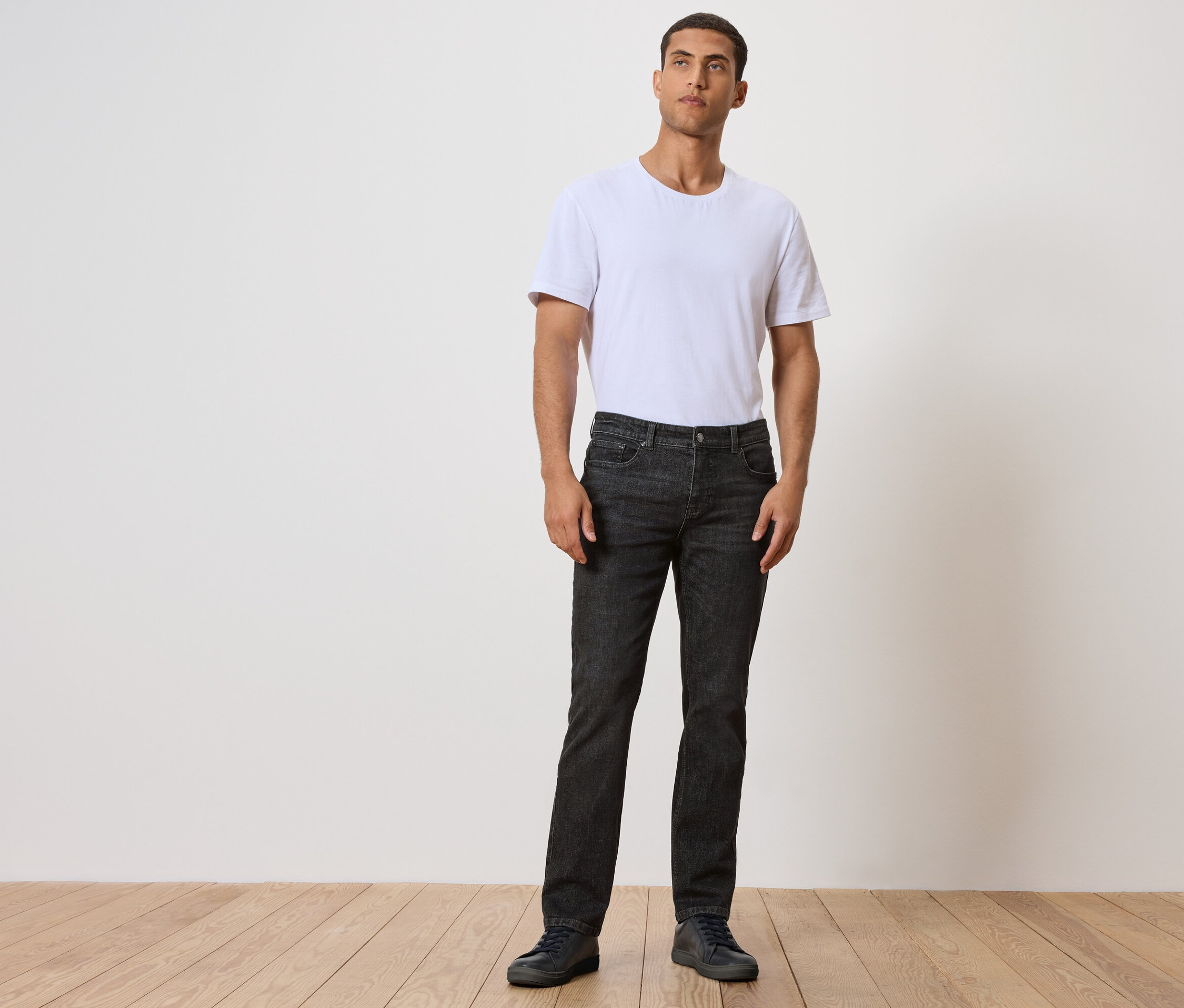 Férfi áll a fapadlón, fekete farmerben és fehér pólóban.