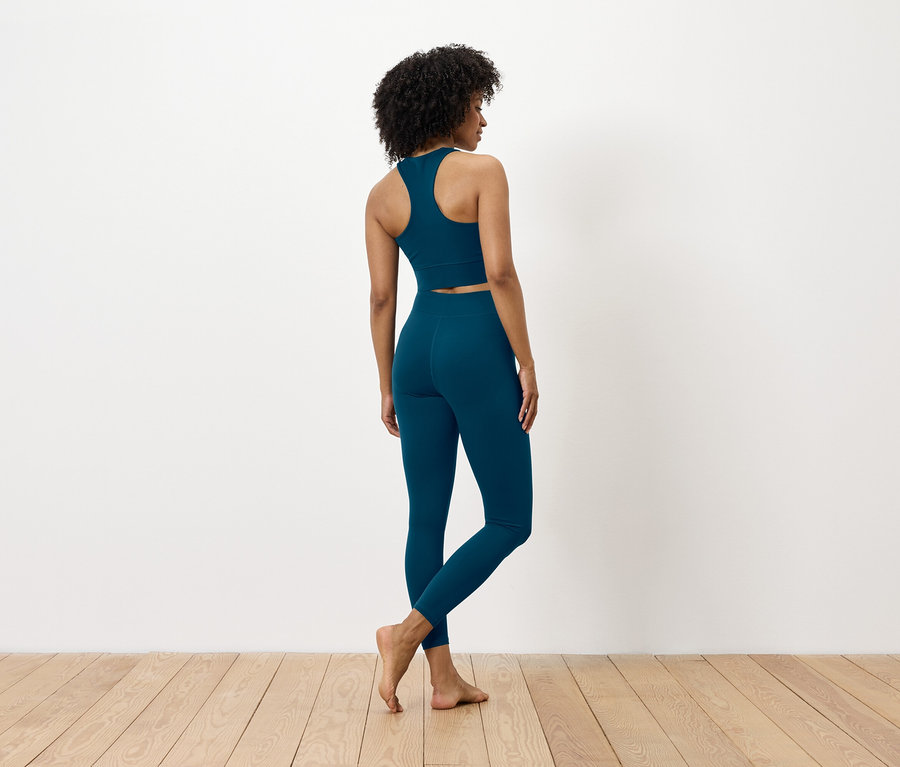 Hátulról látható egy sötét hajú nő, aki kék sportmelltartót és leggingst visel.