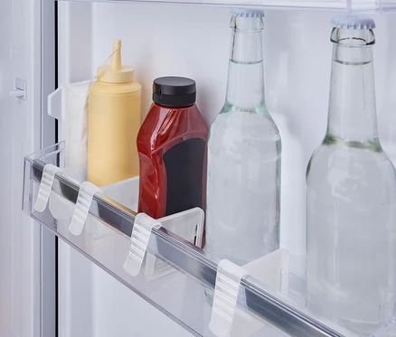A hűtő polcán egy sárga mustáros üveg, egy piros ketchupos üveg és két üveg vizes palack áll.