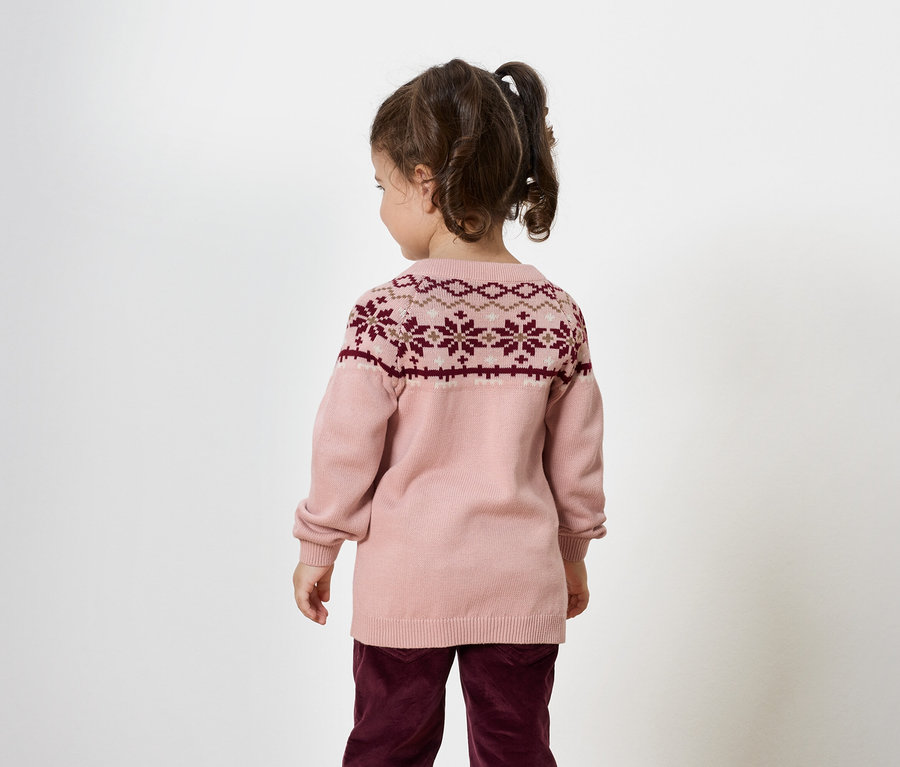 Kislány hátulról, rózsaszín pulóvert visel bordó mintával és bordó nadrágot.