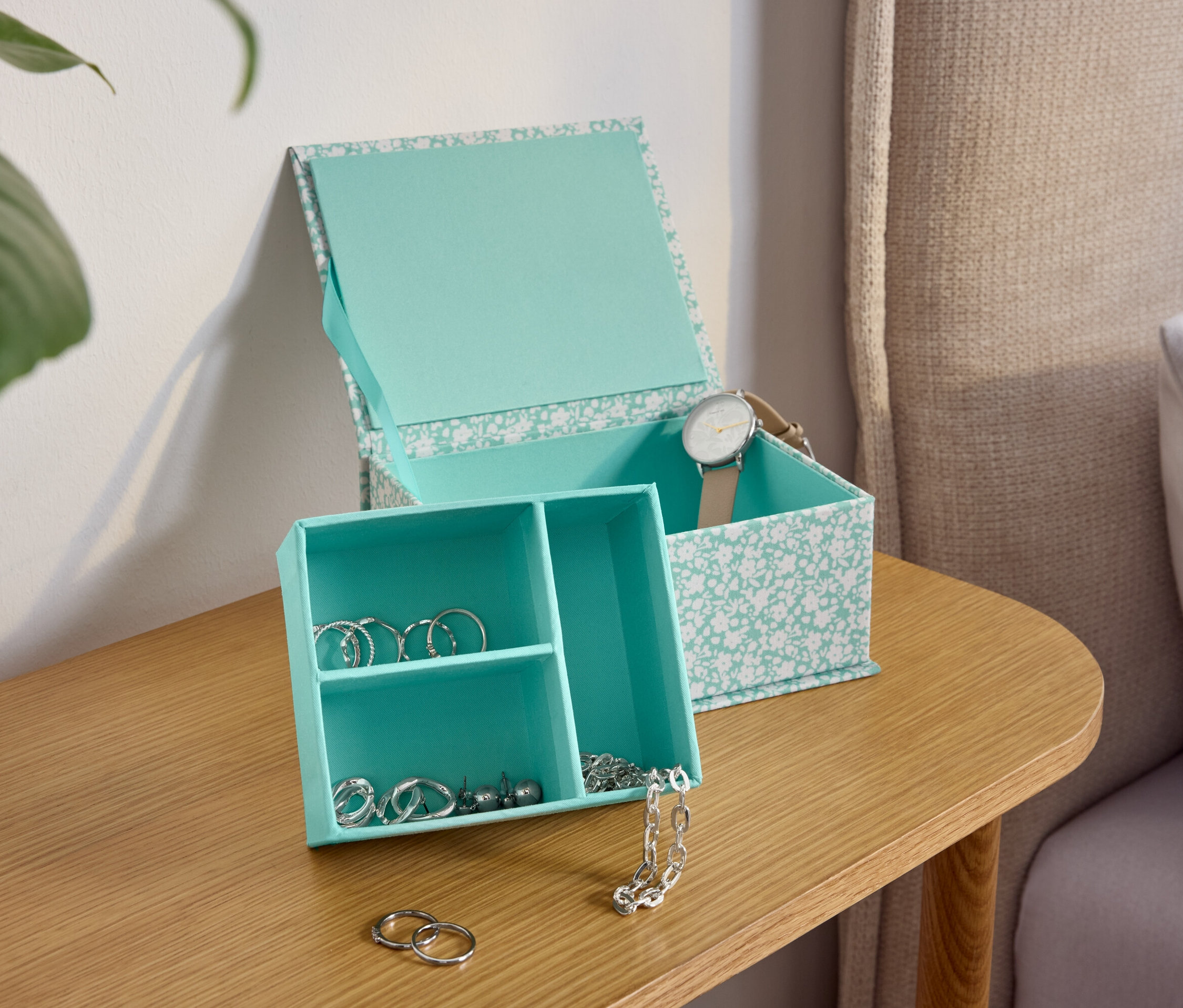 Türkiz virágmintás ékszerdoboz egy fa asztalon az ágy mellett.