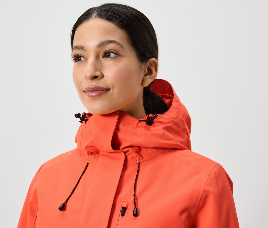 Portré egy nő korall színű, kapucnis kabátban.