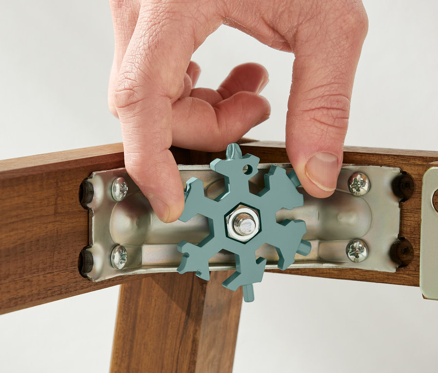 Egy kéz egy multifunkciós kulcsot tart egy csavaron egy fa kereten.