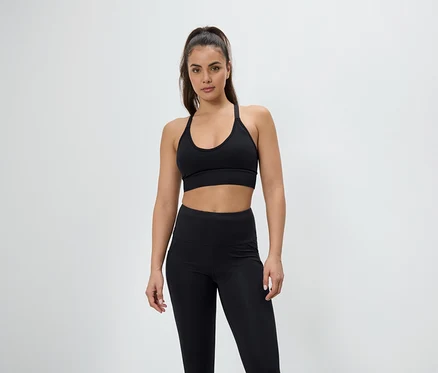 Nő pózol fekete sportmelltartóban és leggingsben.
