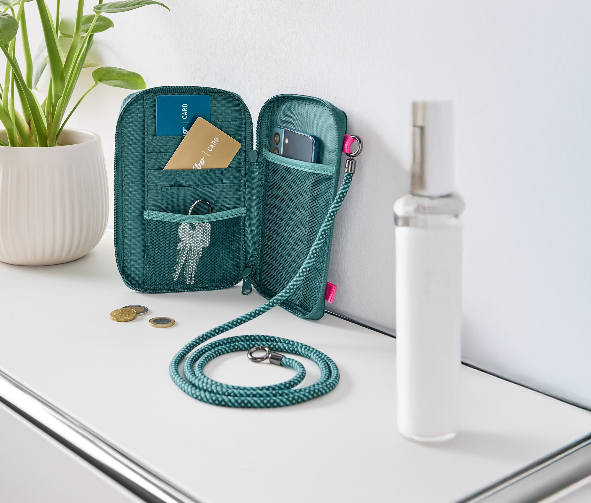 Egy nyitott, zöld pénztárca fekszik egy fehér asztalon, tele kártyákkal, kulcsokkal és egy mobiltelefonnal.