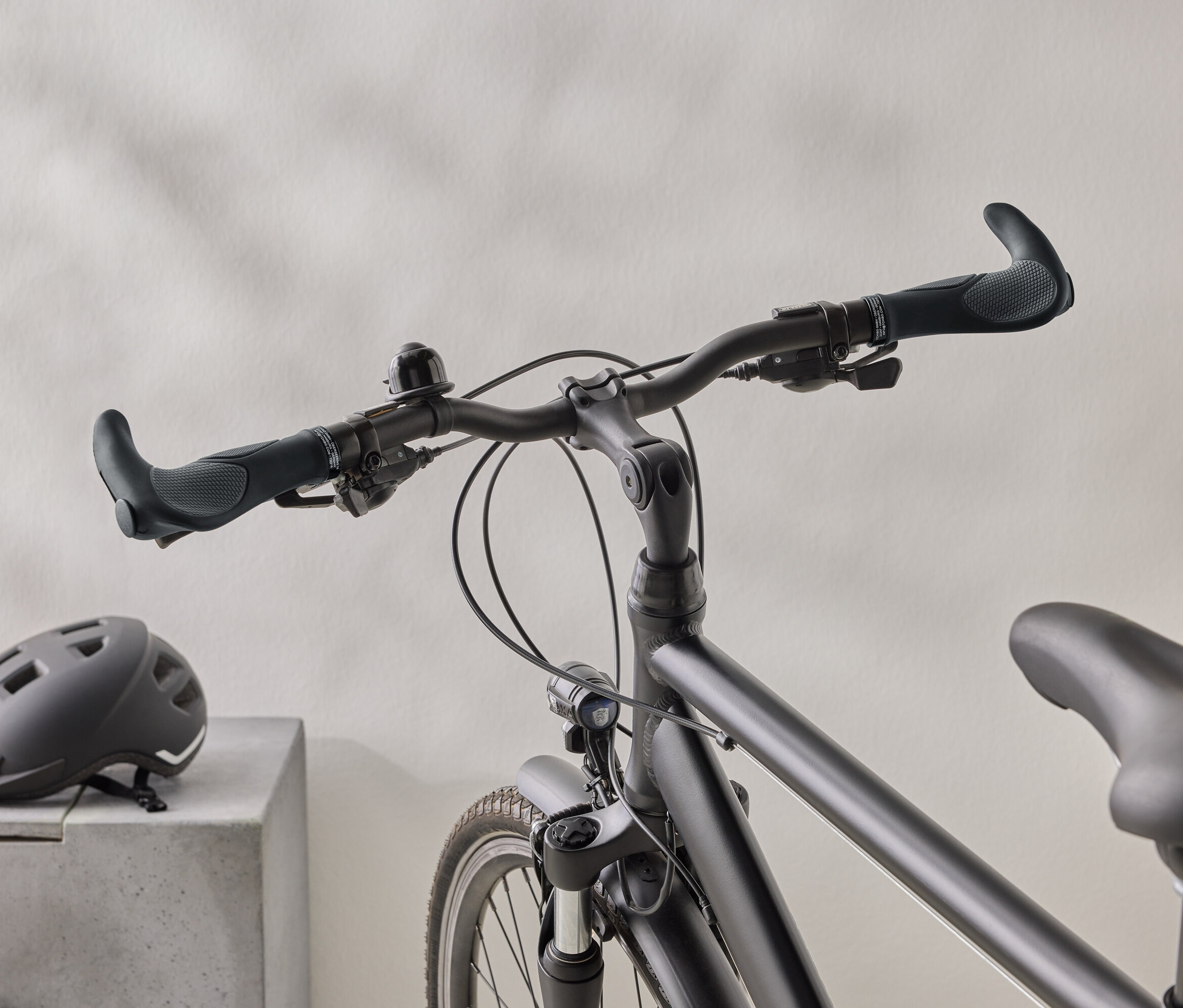 Egy matt fekete kerékpár közeli képe, fekete sisakkal egy betonfelületen a háttérben.