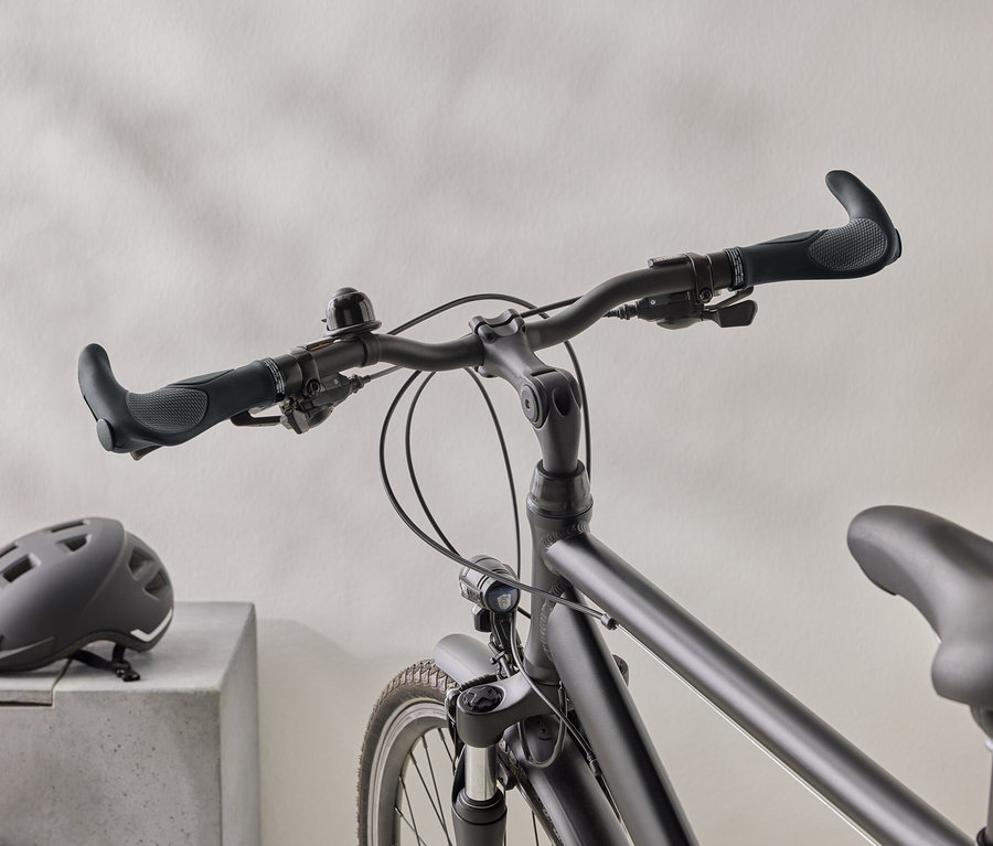 Egy matt fekete kerékpár közeli képe, fekete sisakkal egy betonfelületen a háttérben.