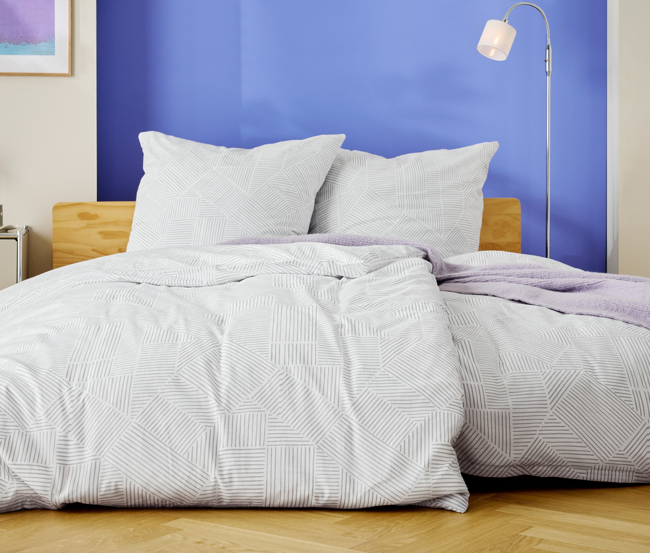 Egy ágy fehér ágyneművel, geometrikus mintával és két párnával, egy kék fal előtt.