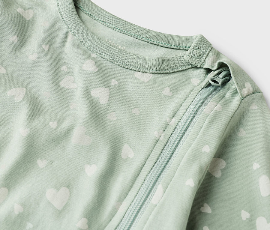 Közeli kép egy világoszöld, fehér szív mintás, cipzáras baba hálózsákról.