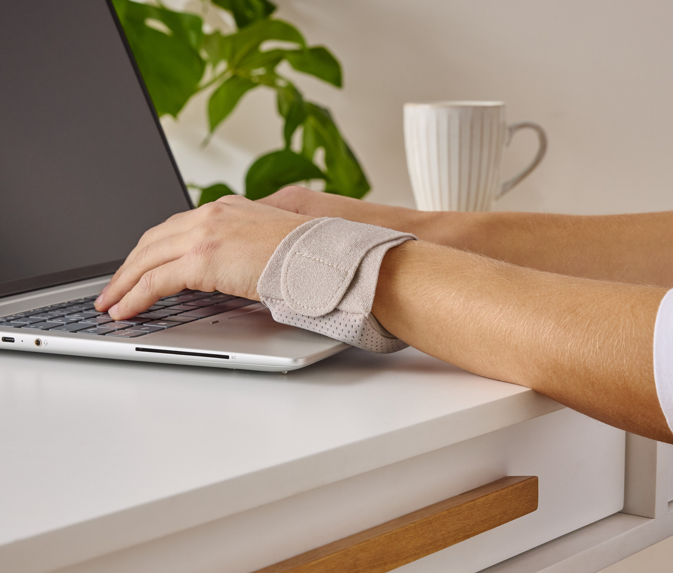 Egy személy laptopon gépel és csuklótámaszt visel.