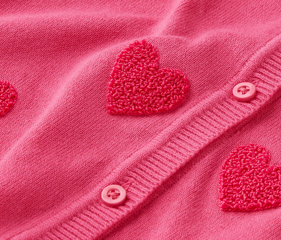 Egy rózsaszín kardigán közelképe szív alakú rátétekkel és gombokkal.