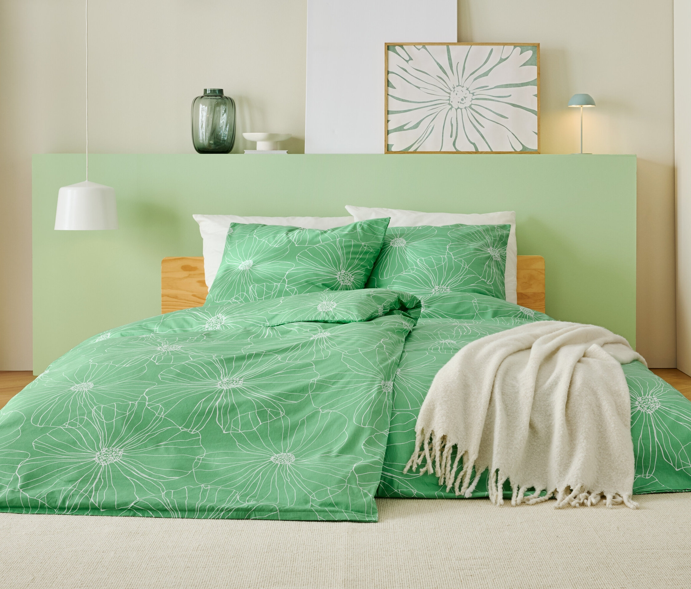 Ágy zöld ágyneművel, fehér virágmintával, fehér takaróval és világoszöld fejtámlával.