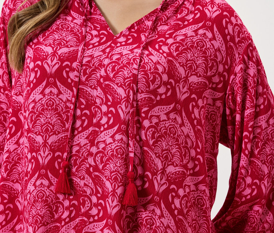 Egy piros, rózsaszín virágmintás, húzózsinóros felső közeli képe.