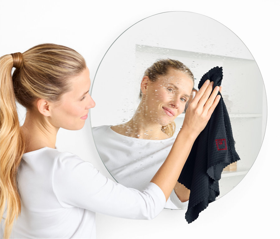 Nő fekete kendővel tisztít egy kerek tükröt.