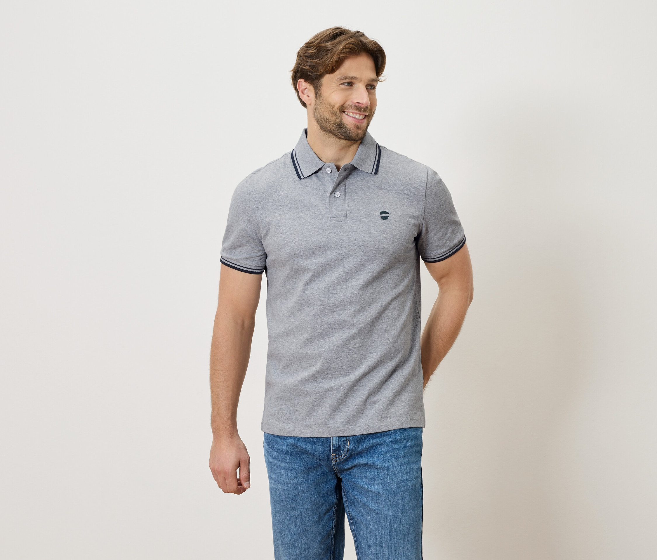 Szürke pólóinget és farmert viselő férfi áll semleges háttér előtt.