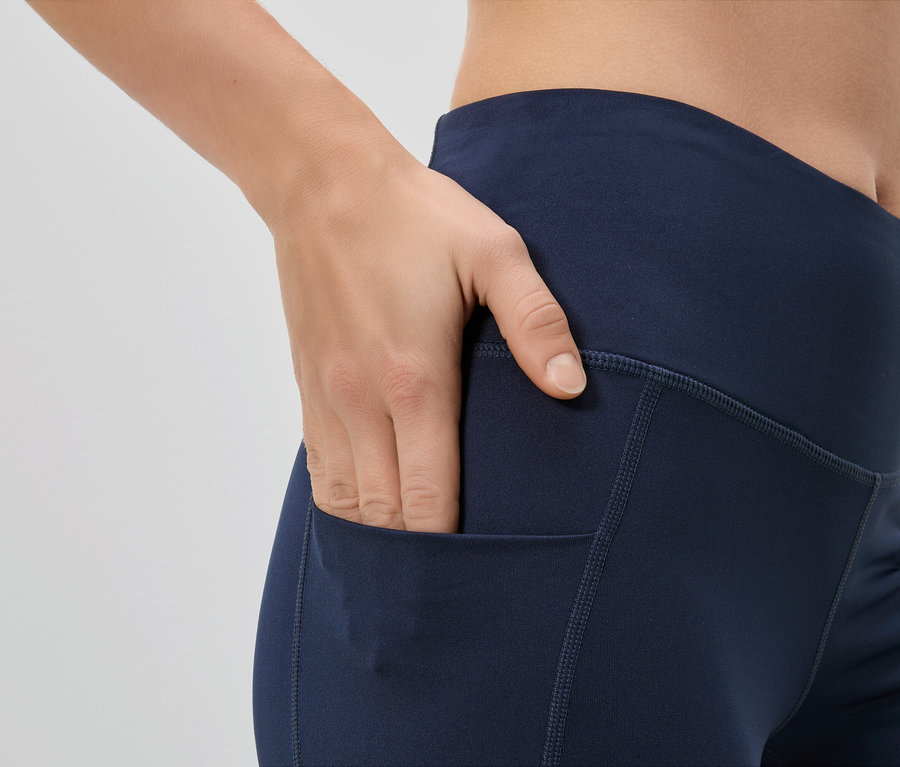 Nő teszi a kezét egy sötétkék leggings zsebébe.