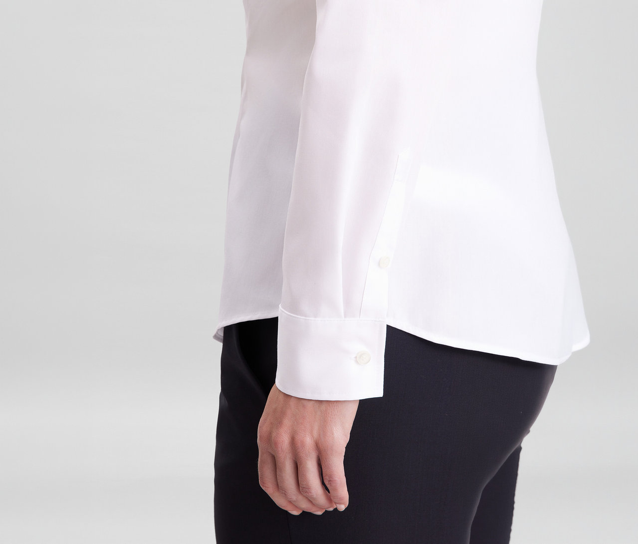 Egy személy fehér Seidensticker slim fit szabású, vasalást nem igénylő ingblúzban és fekete nadrágban, látszik az ingujj mandzsettája.