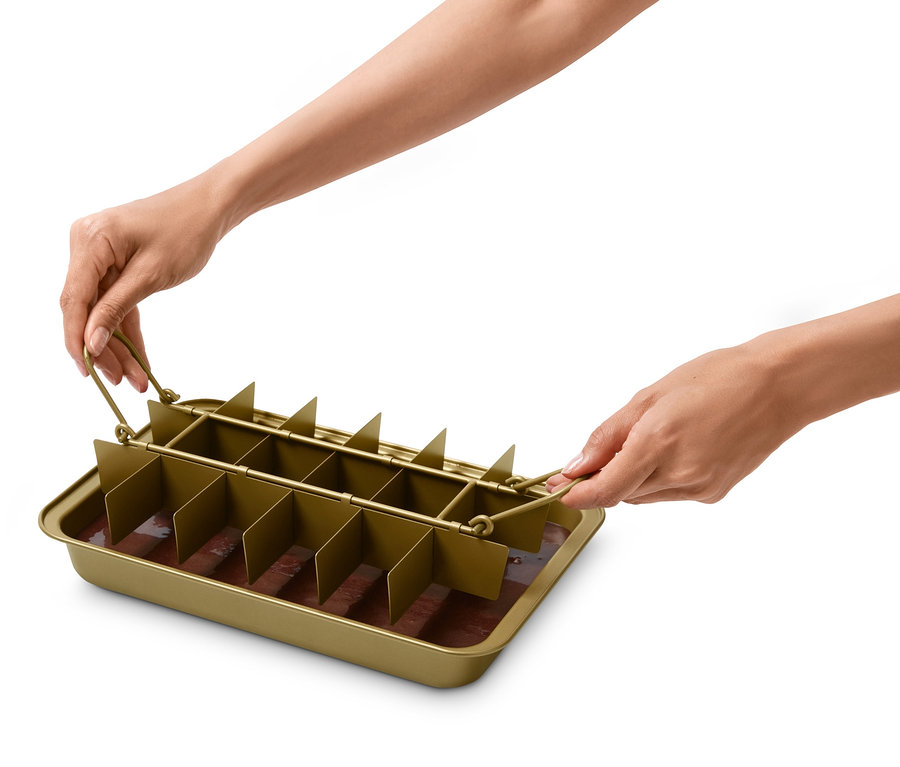 Kezek tartanak egy brownie sütőformát, benne barna keverékkel.
