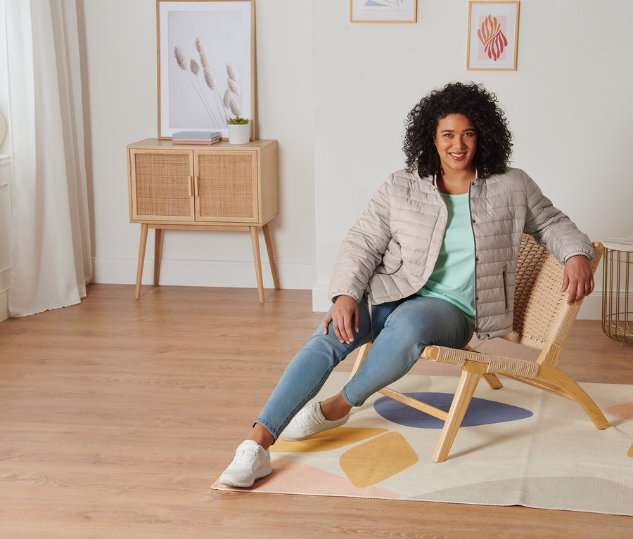 Nő ül egy széken, és menta színű, 3/4-es ujjú felsőt, treggingst, velúrbőr sneaker cipőt és bézs steppelt dzsekit visel.