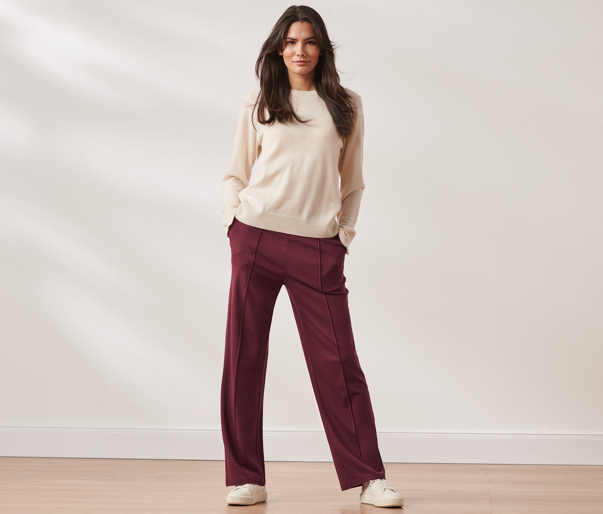 Nő áll, kezét a zsebében tartja, és női lezser nadrág, bordó színű nadrágot visel.