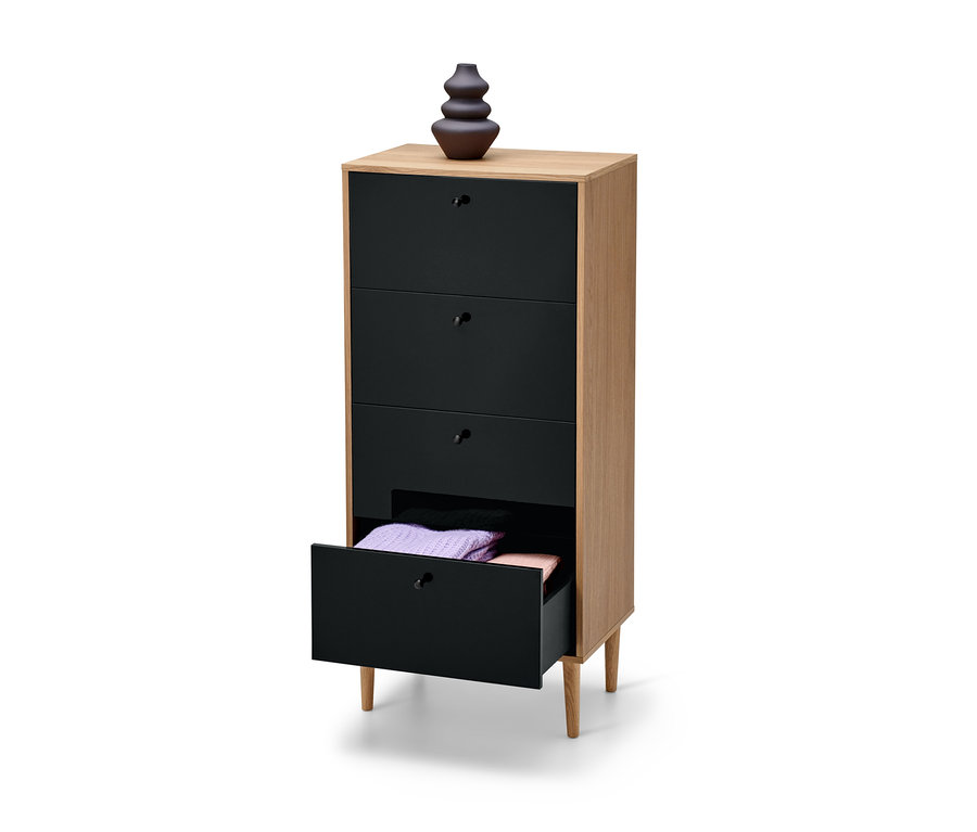 Magas, keskeny, antracit színű "Bekeson" komód négy fiókkal, melyből az egyik nyitva van, benne összehajtott pulóverekkel. A komódon egy barna váza áll.