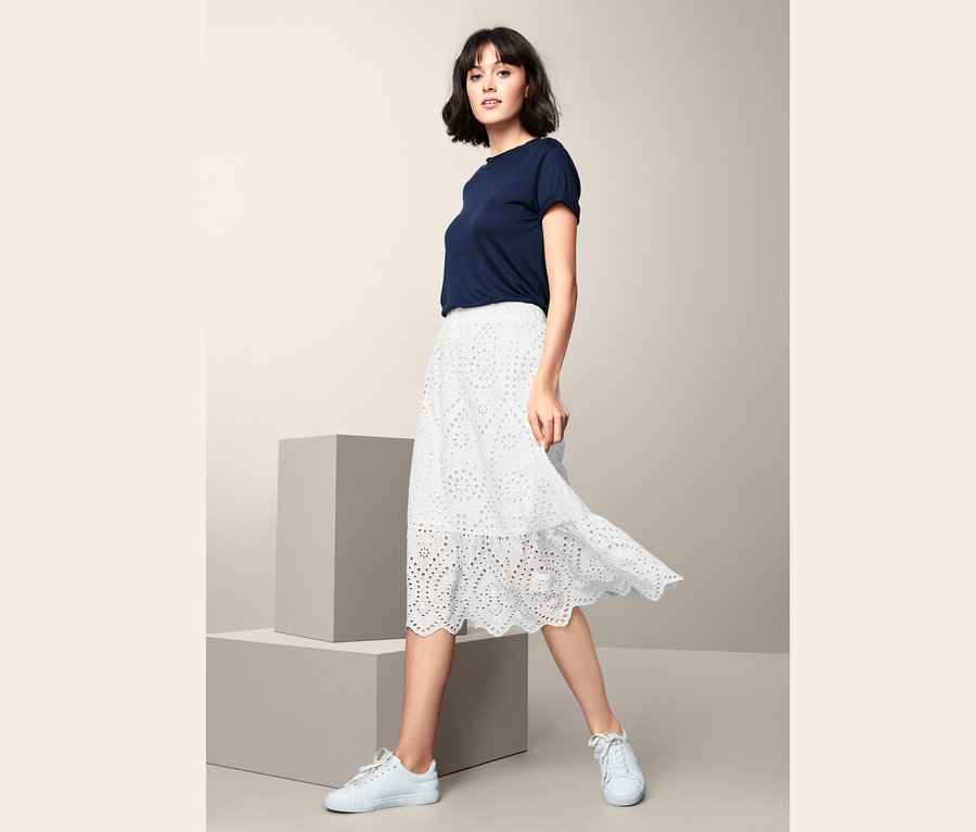 Nő pózol fehér, lyukhímzéses szoknyában.