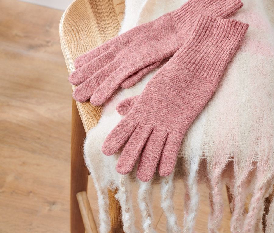 Rózsaszín, gyapjú kötött kesztyű egy fa széken, fehér kendővel.