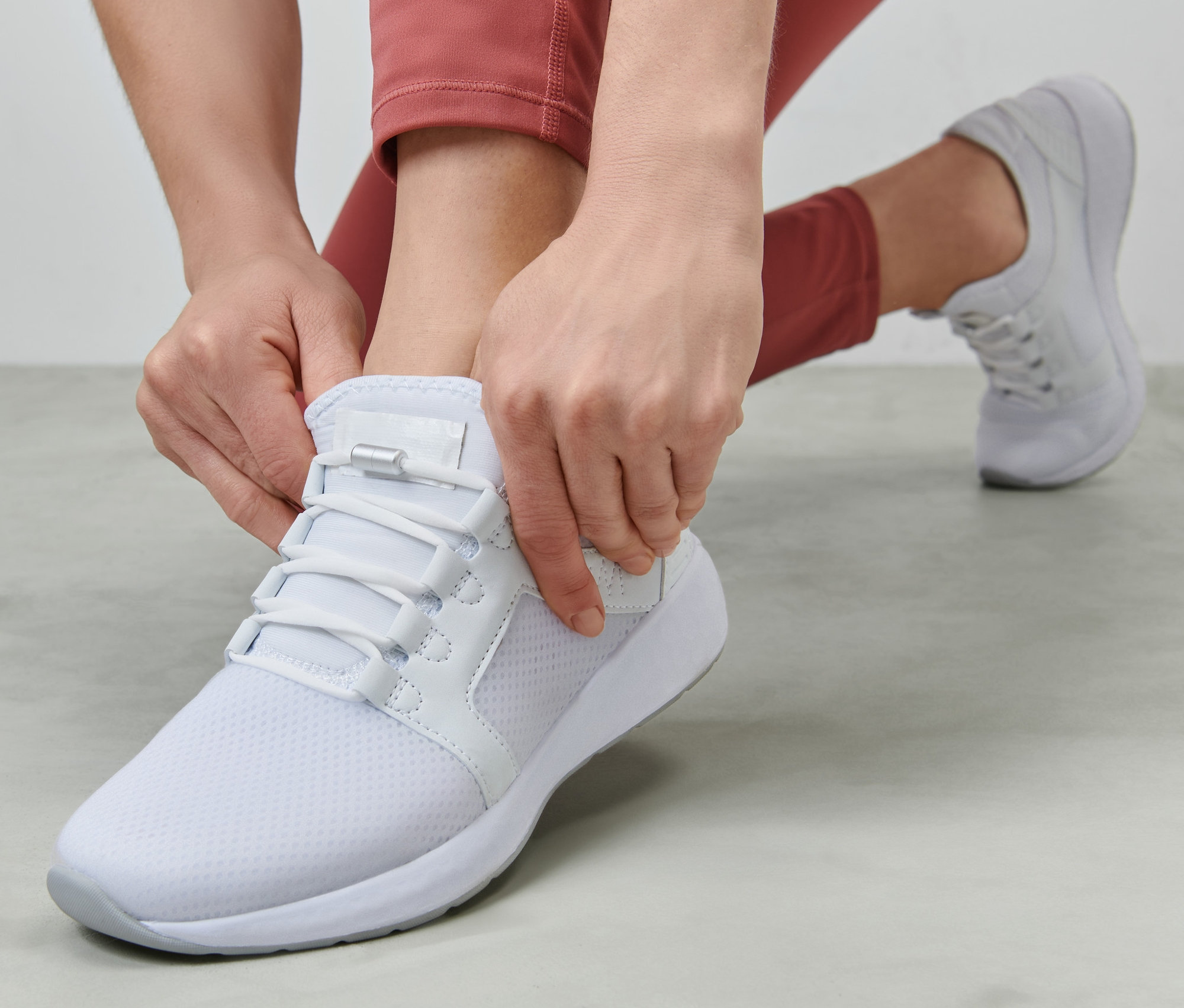 Nő fűzi az elasztikus cipőfűzőt egy fehér cipőn.
