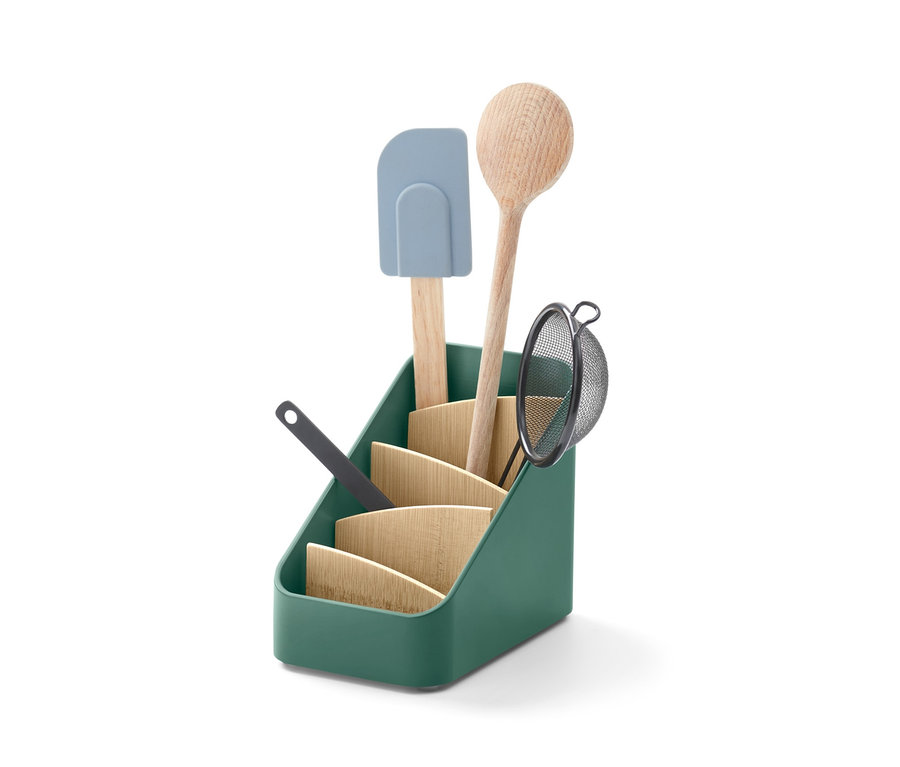 A zöld kiegészítőtartóban egy fakanál, egy szűrő és egy spatula látható.