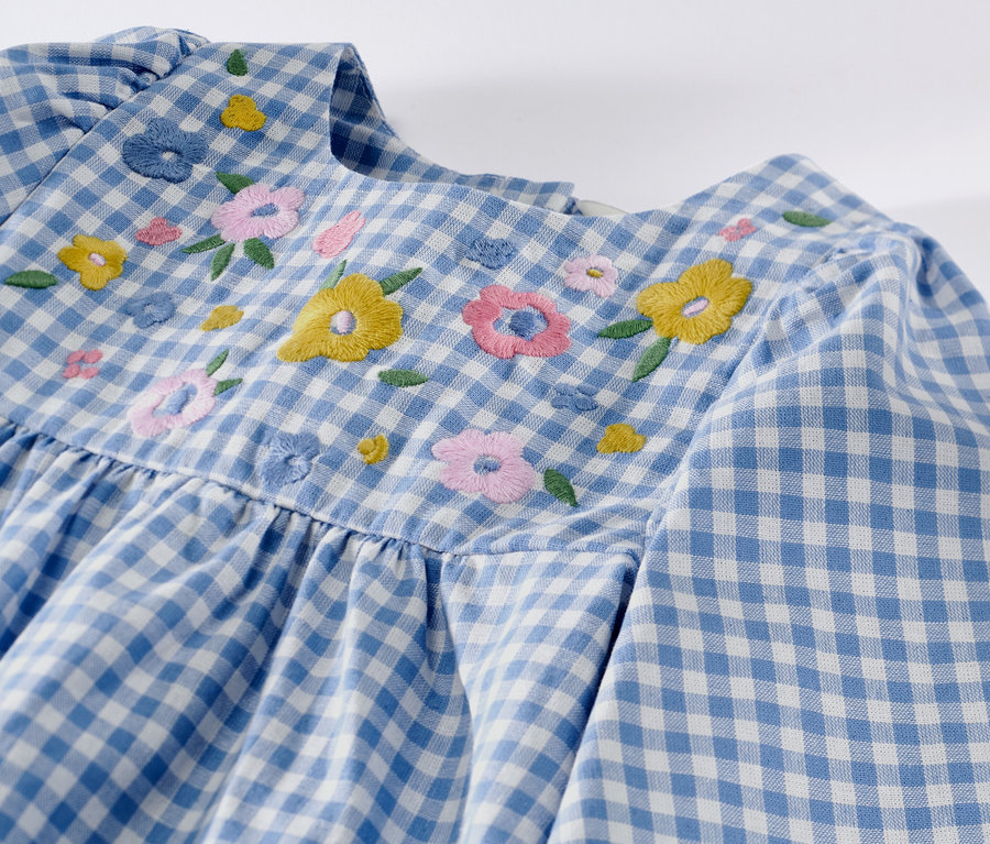 Kislány szövött ruha részlete kék-fehér kockás mintával és virág hímzéssel.