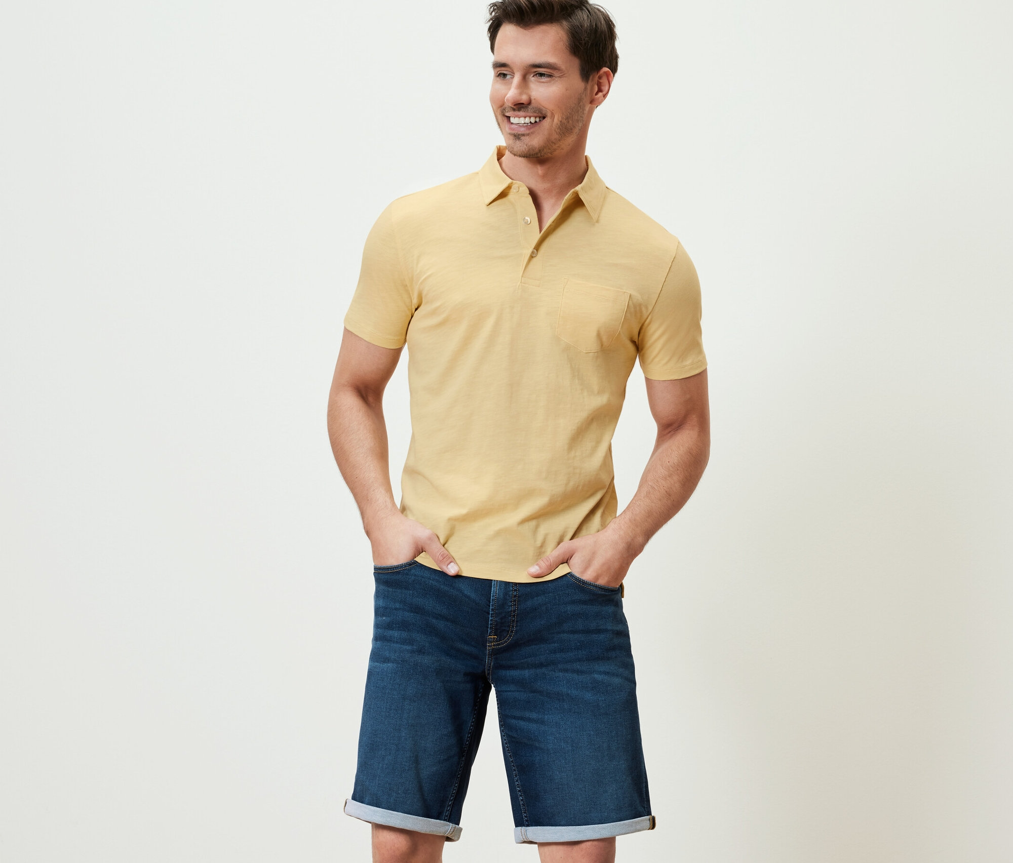 Férfi pózol melírozott sárga jersey pólóingben és farmer rövidnadrágban.