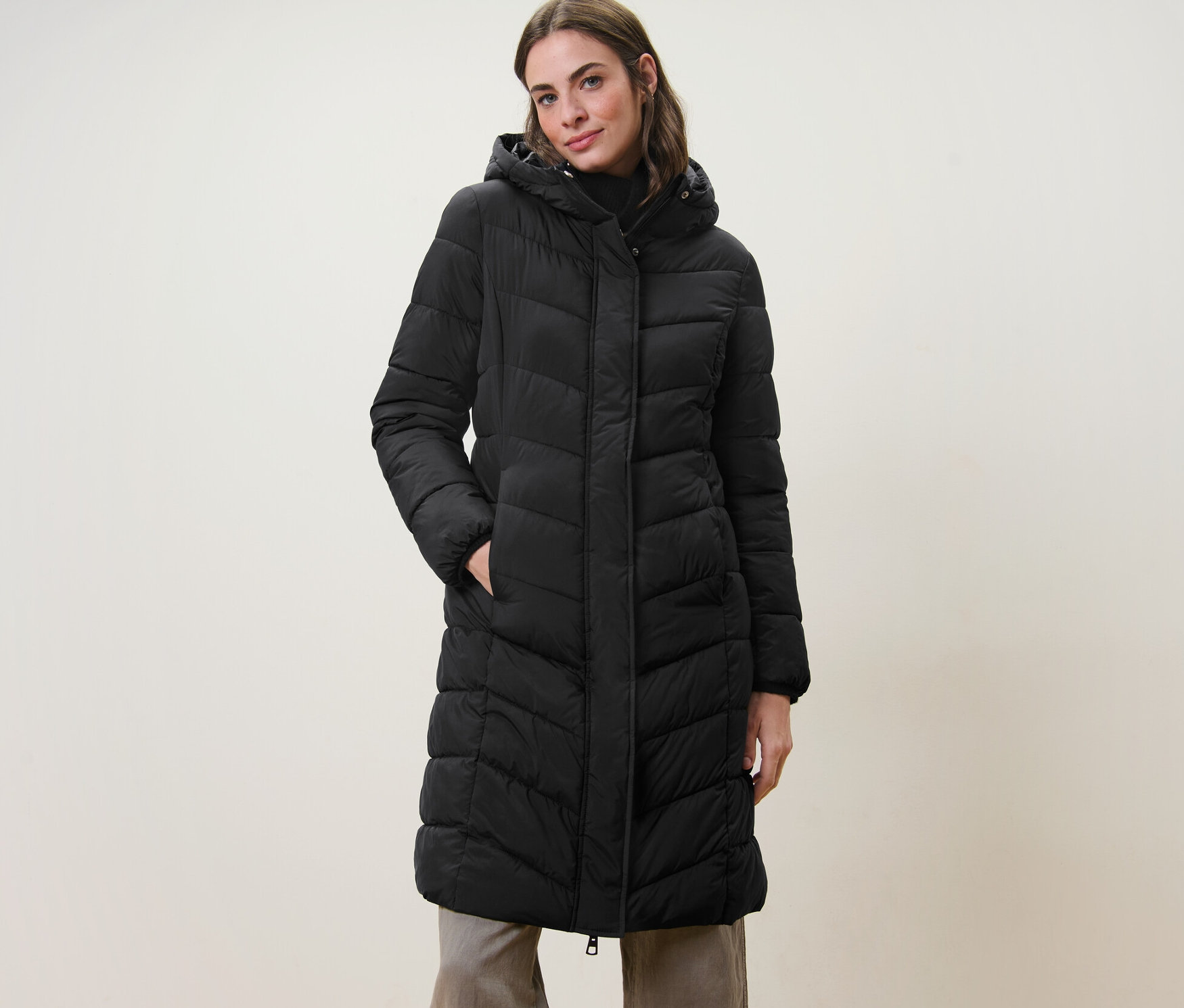 Nő pózol fekete, steppelt, kapucnis kabátban.