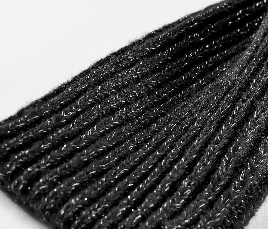 Női kötött csuklómelegítő, csillogó, fekete színben, közeli kép.