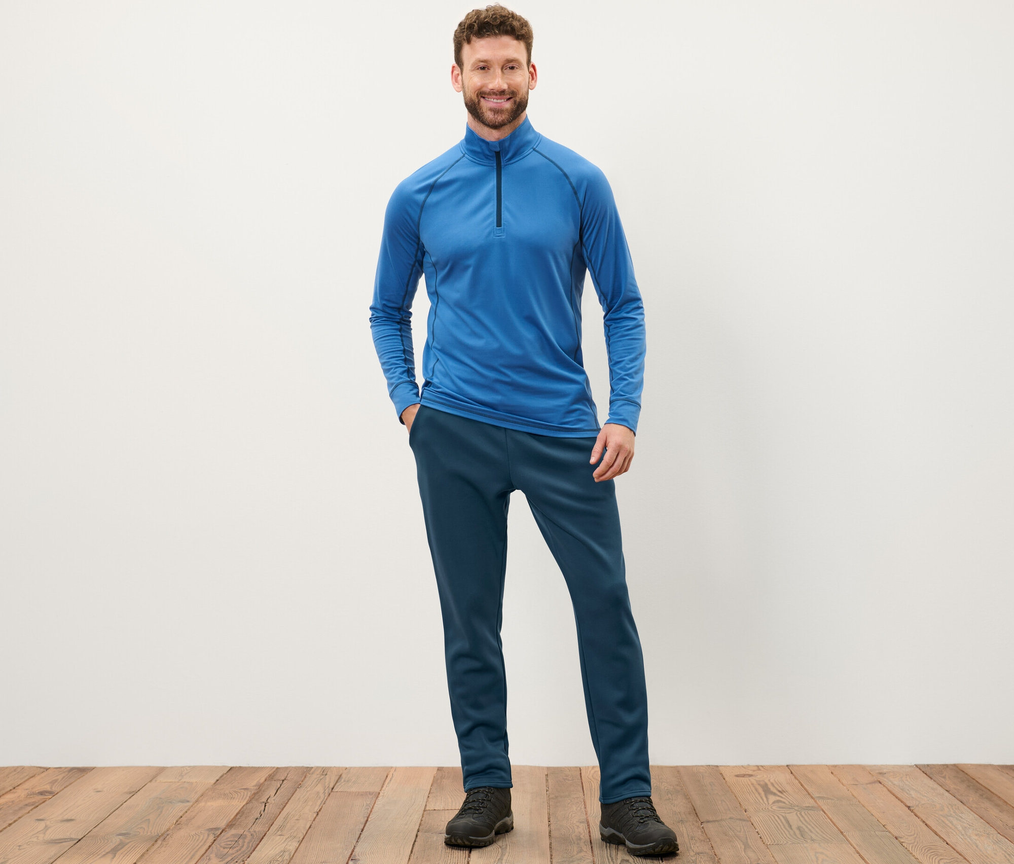 Férfi áll kék felsőben és sötétkék funkcionális bélelt tréningnadrágban.