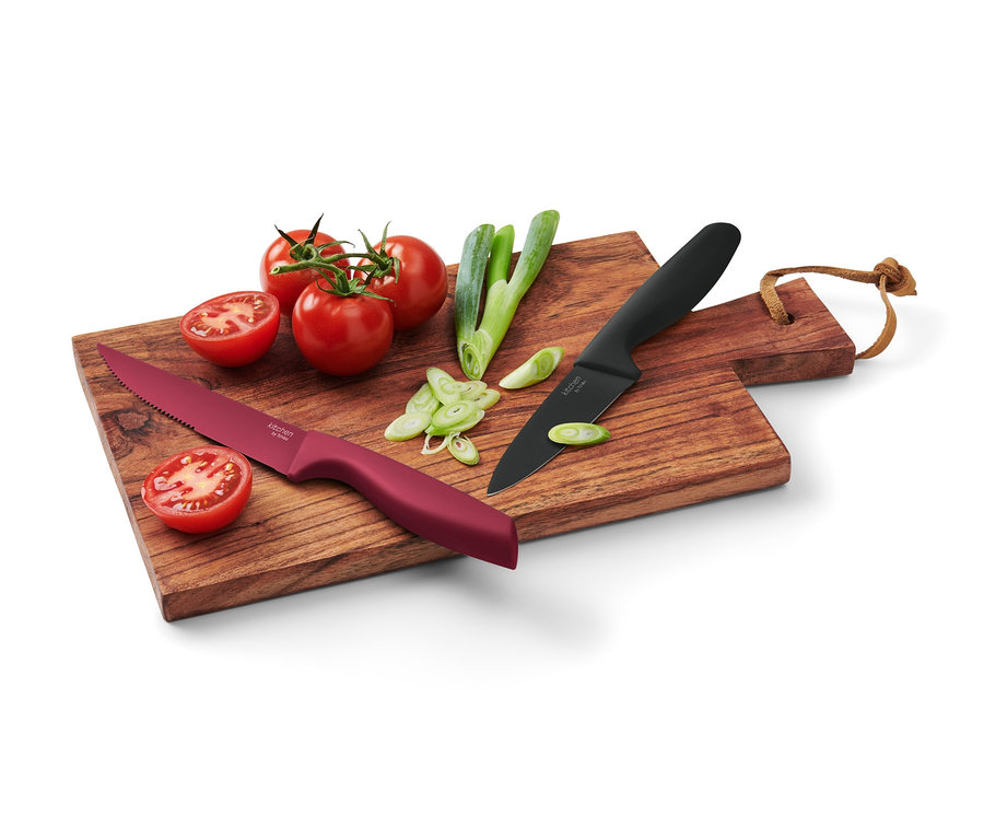 Egy fa vágódeszkán két konyhai kés, paradicsom és felvágott zöldhagyma látható.