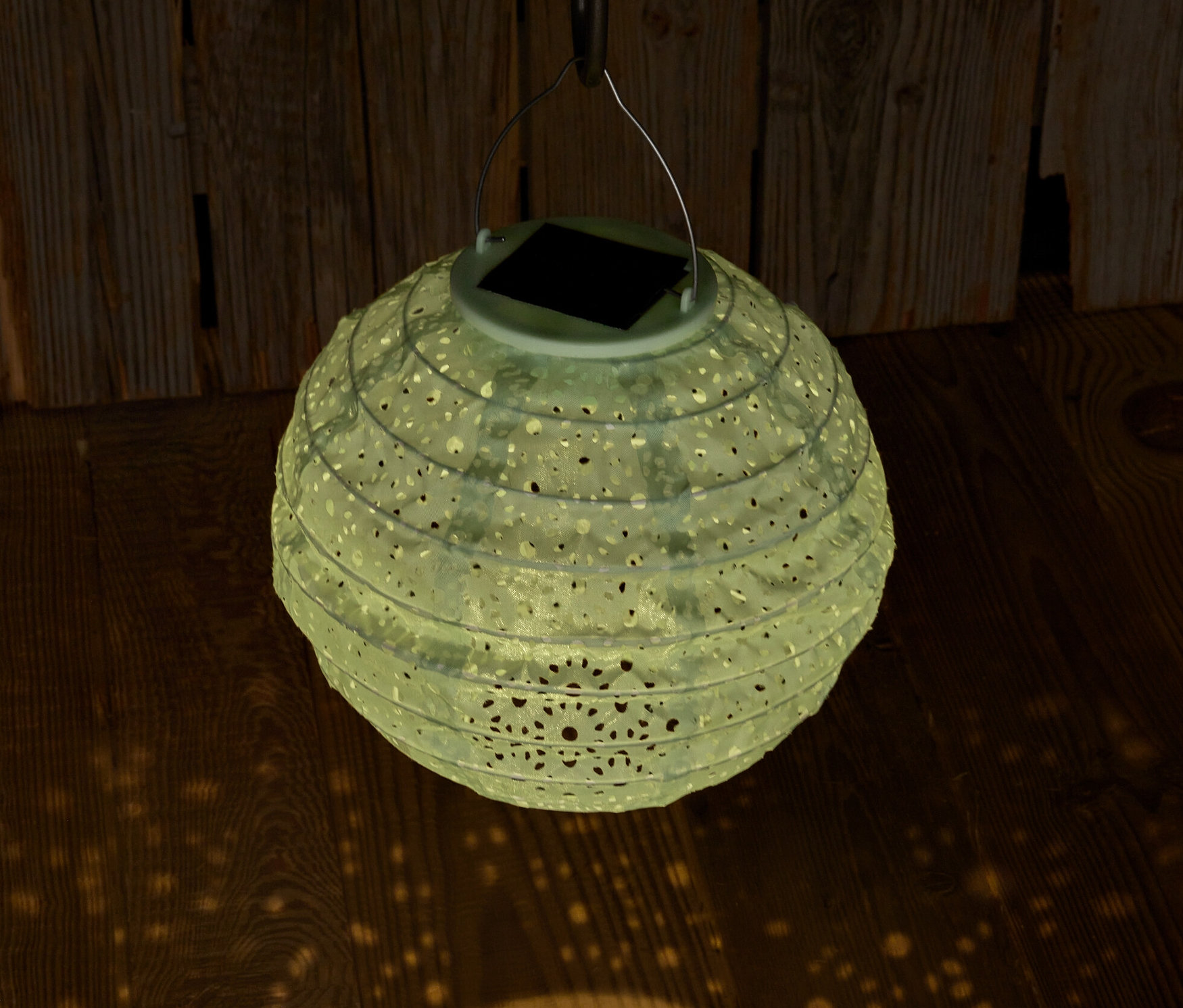 A lógó, dekoratív lyukakkal ellátott napelemes lampion fényt vet a fapadlóra.