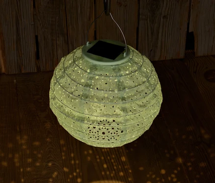 A lógó, dekoratív lyukakkal ellátott napelemes lampion fényt vet a fapadlóra.