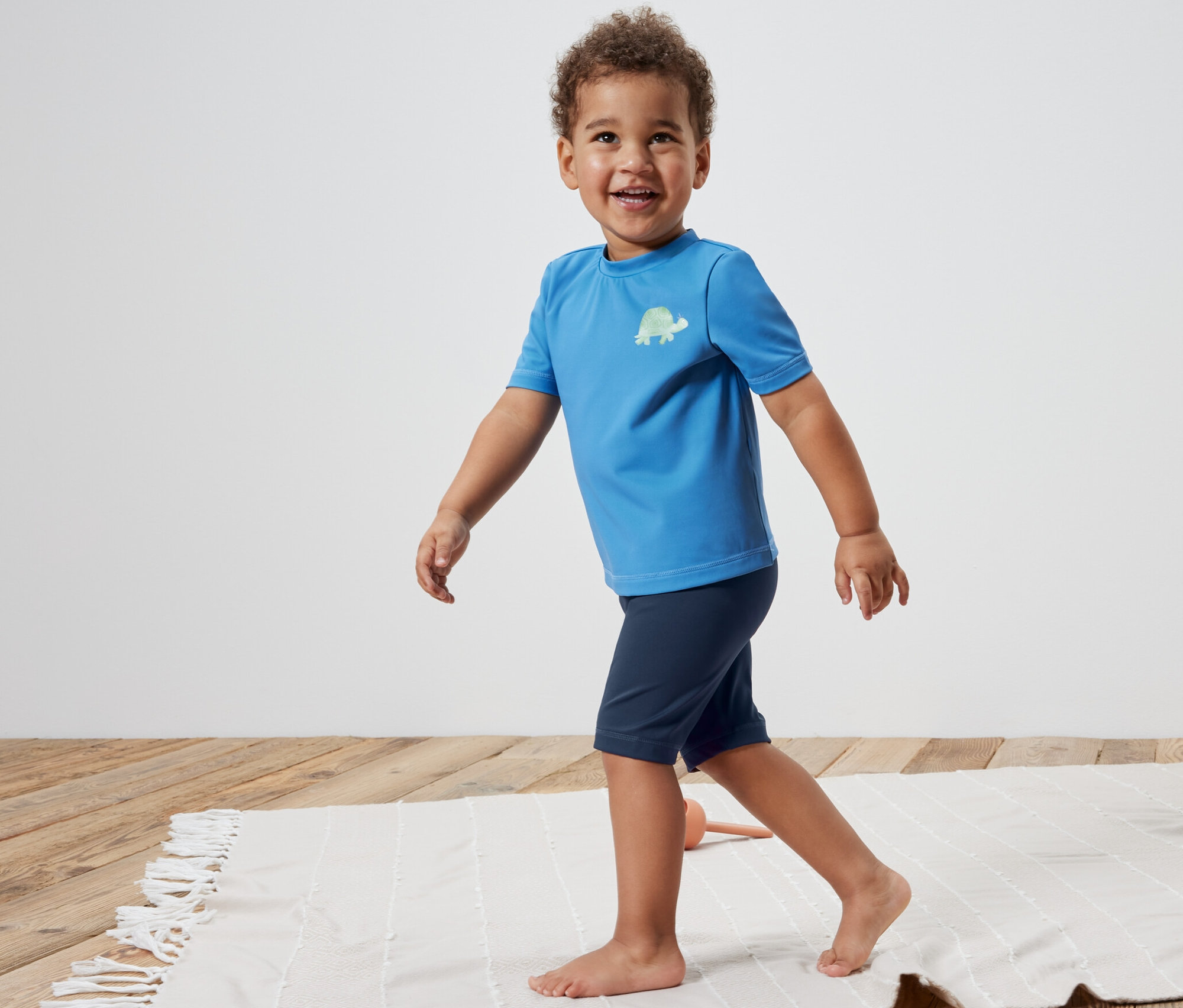 Fiú sétál a strandon Kisgyerek UV-szűrős úszónadrágban.