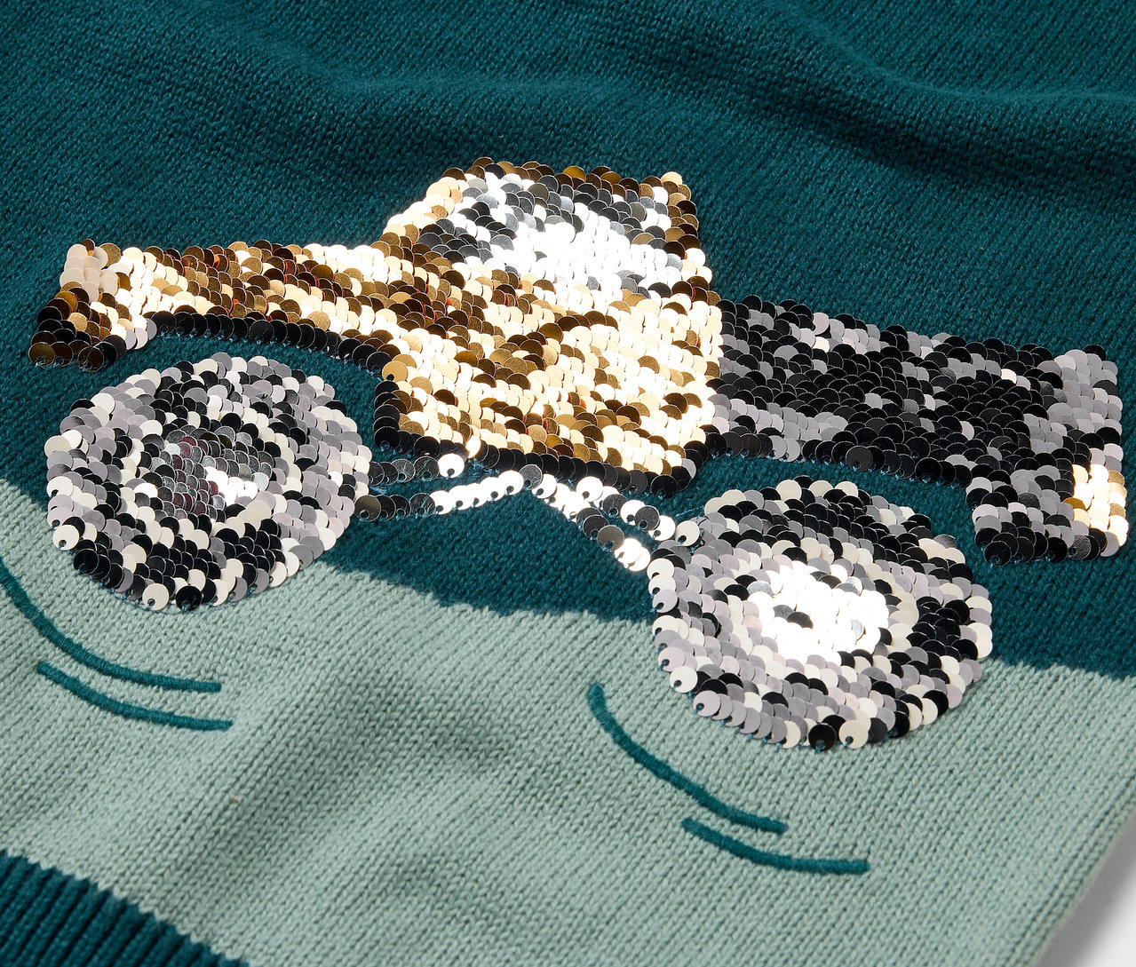 Egy gyermek kötött pulóver közeli képe, flitteres teherautó mintával.