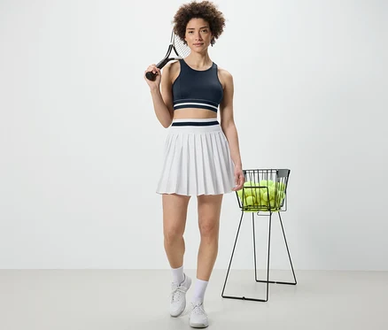 Nő teniszütőt tart és kék »Crop Top« sportmelltartót visel.