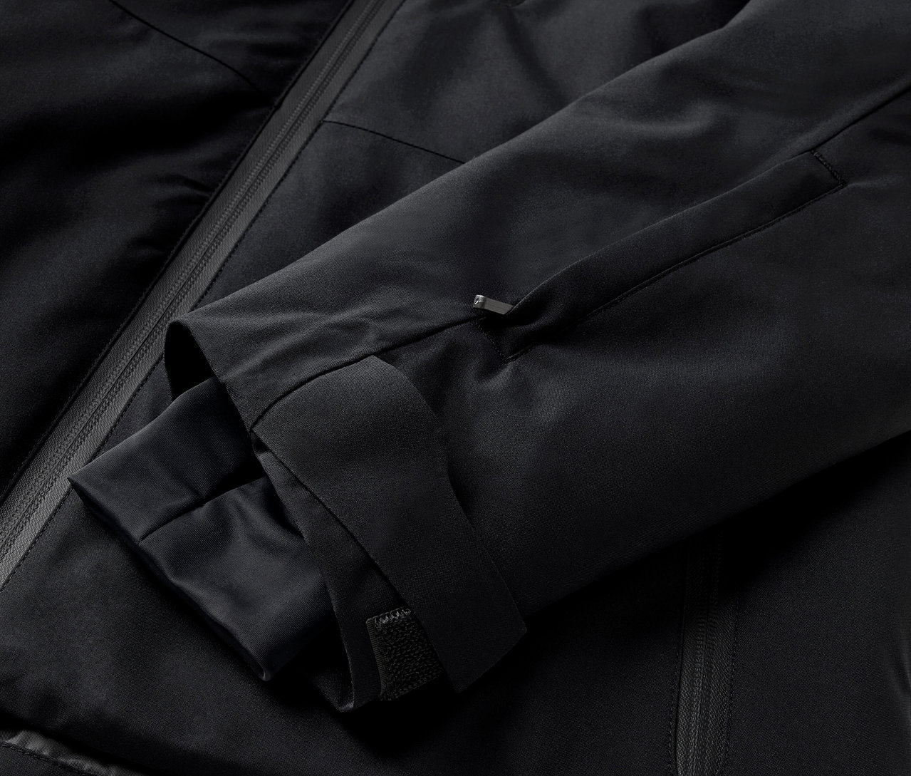 Egy fekete kabát részlete, ujjal és cipzáras zsebbel.