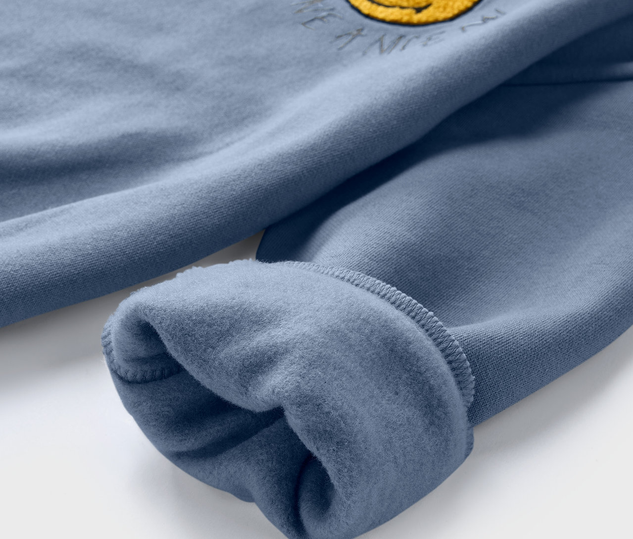 Kék SMILEYWORLD® gyerek szabadidőfelső részletgazdag képe, bolyhozott belsővel és sárga mosolygós mintával.