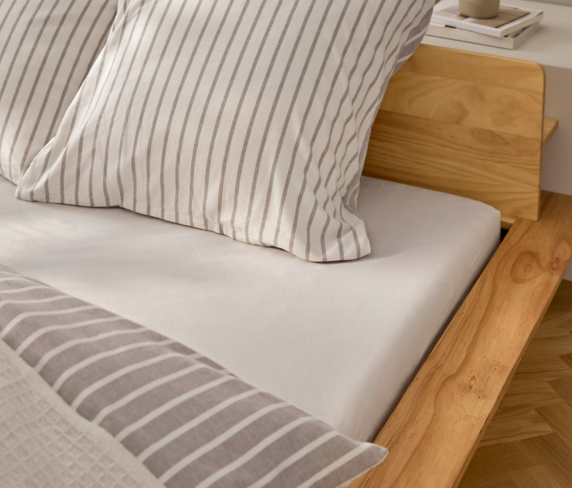 Egy ágy részletének képe fehér lepedővel és szürke csíkos párnákkal.