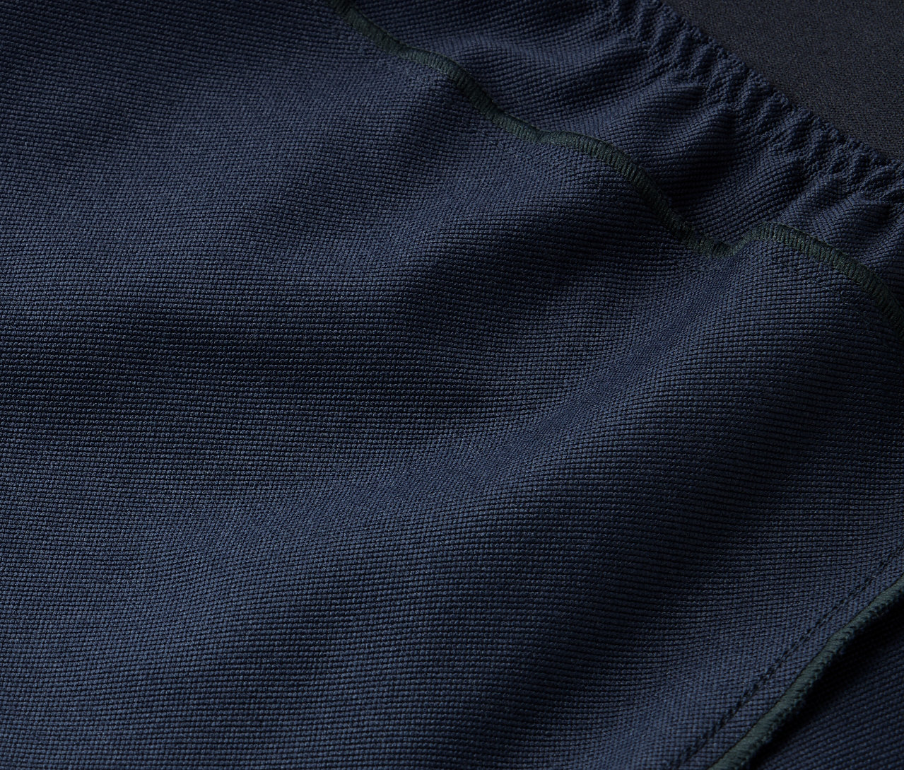 Közelkép egy sötétkék szövet textúrájáról, felül húzózsinórral.
