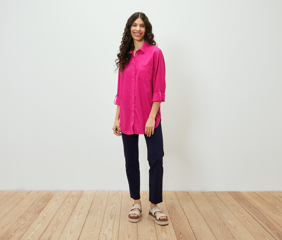 Egy nő áll, és egy rózsaszín, hosszú lenvászon blúzt visel.