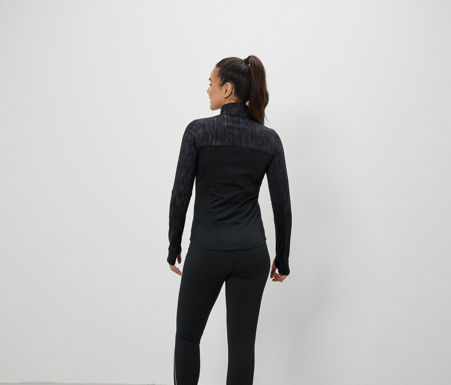 A kamerának háttal álló nő fekete sportruházatot visel.